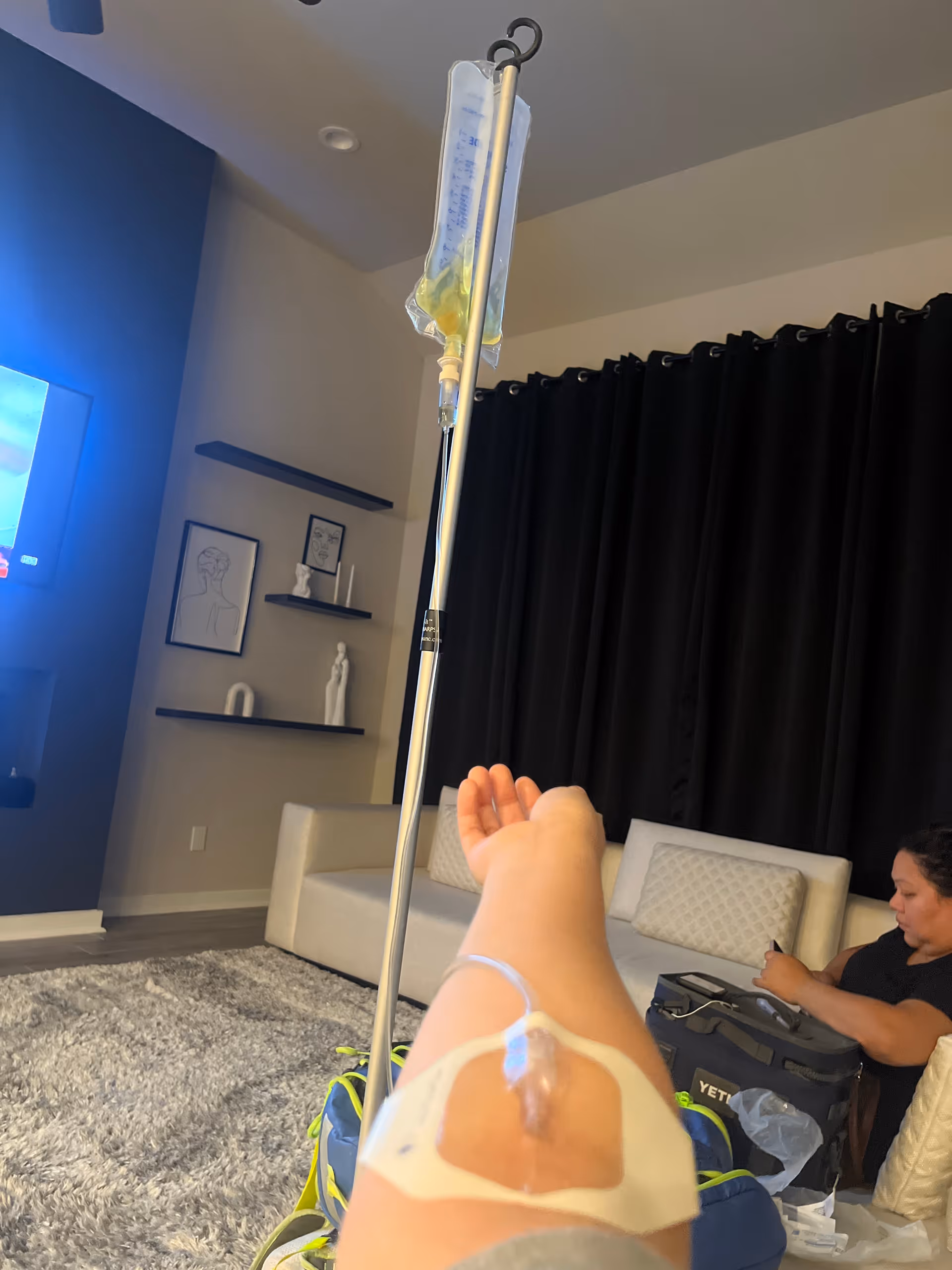 Resident receives IV therapy in a living room with a caregiver nearby.