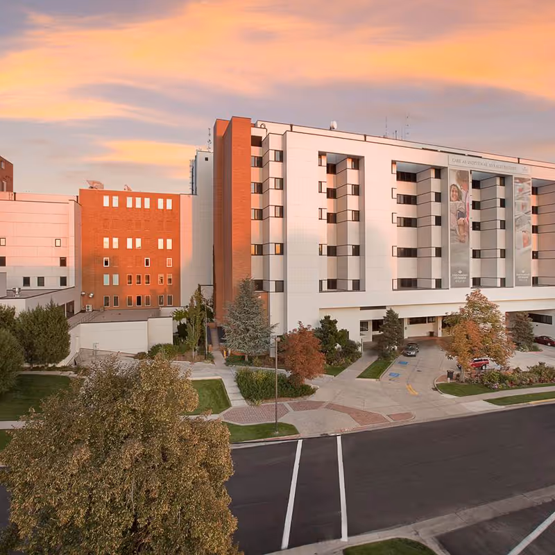 A multi-story medical facility exterior with white and brick facade, entrance, banners, and landscaping.