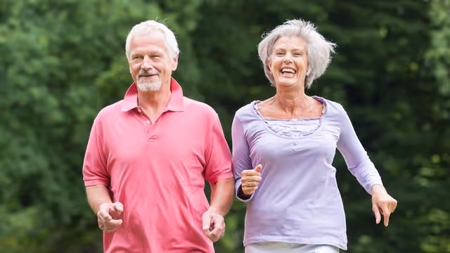 Smiling elderly couple jogging outdoors in a lush green park