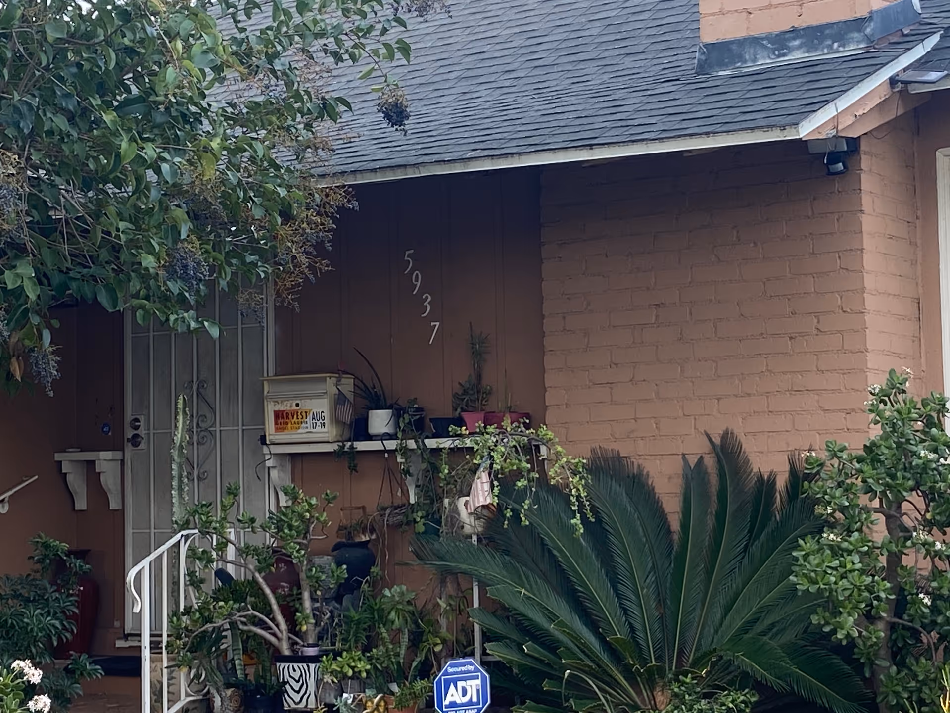 Front entrance with porch plants, security sign, and address numbers on a peach-colored building.