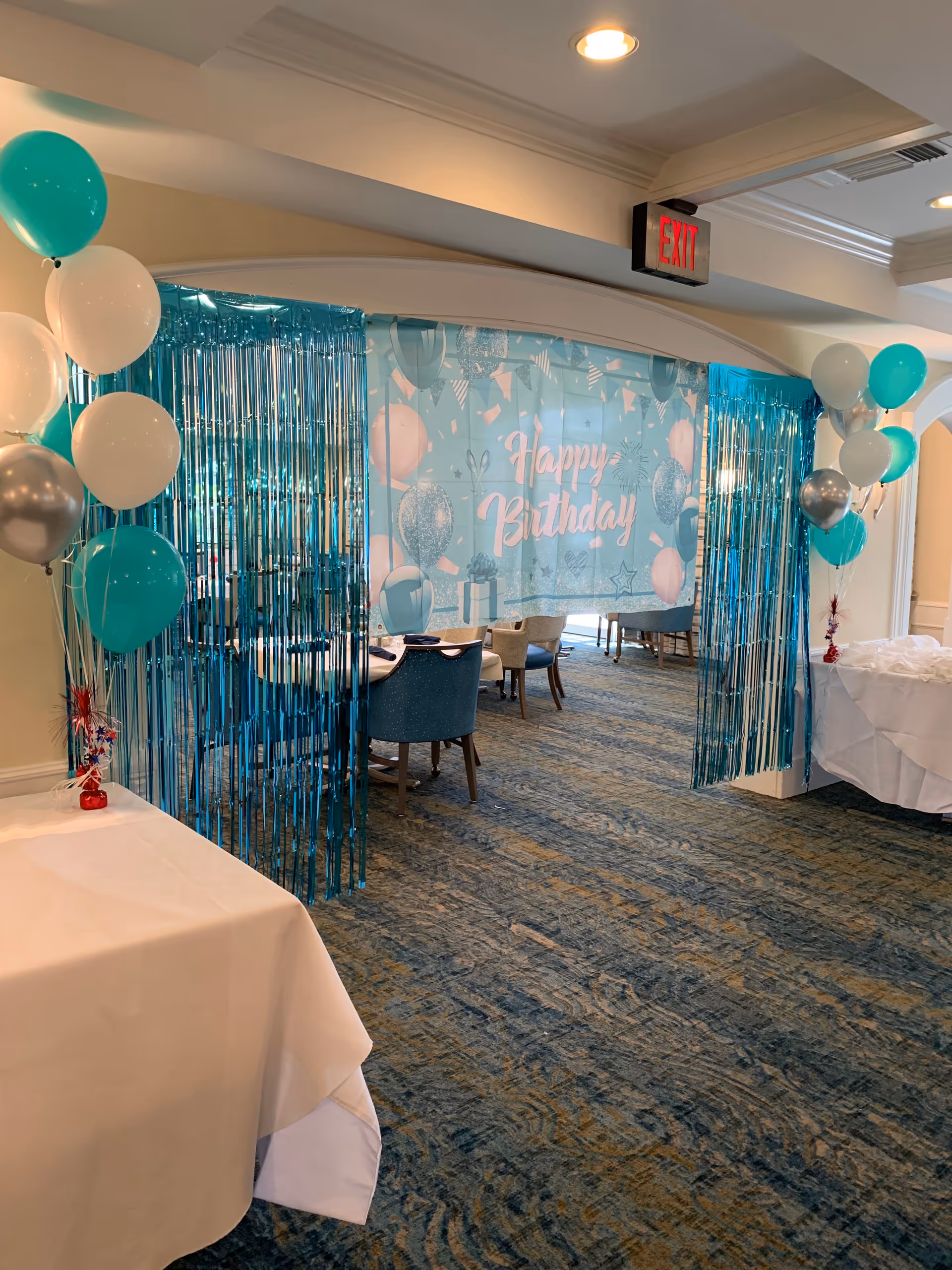 Blue birthday party decor with balloons and fringe curtains in a dining room.