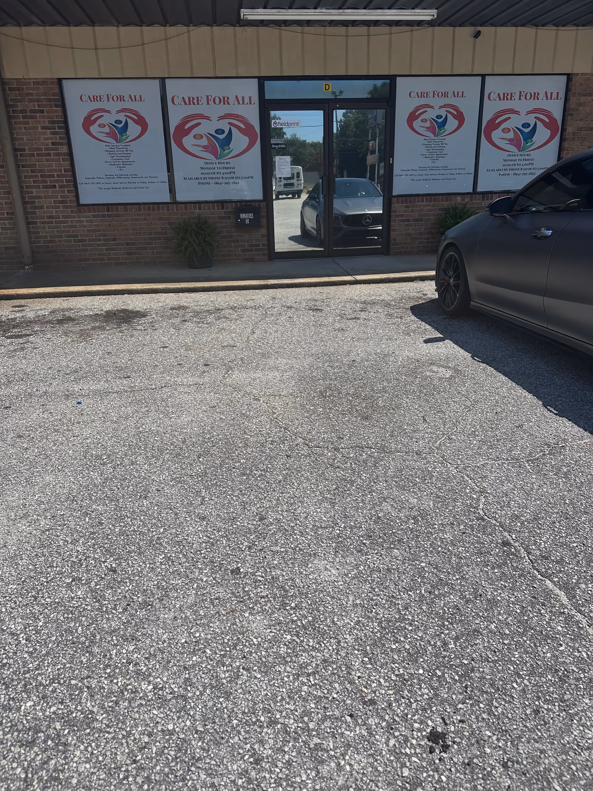 Exterior of CARE FOR ALL LLC facility with large posters on windows and a parked car.