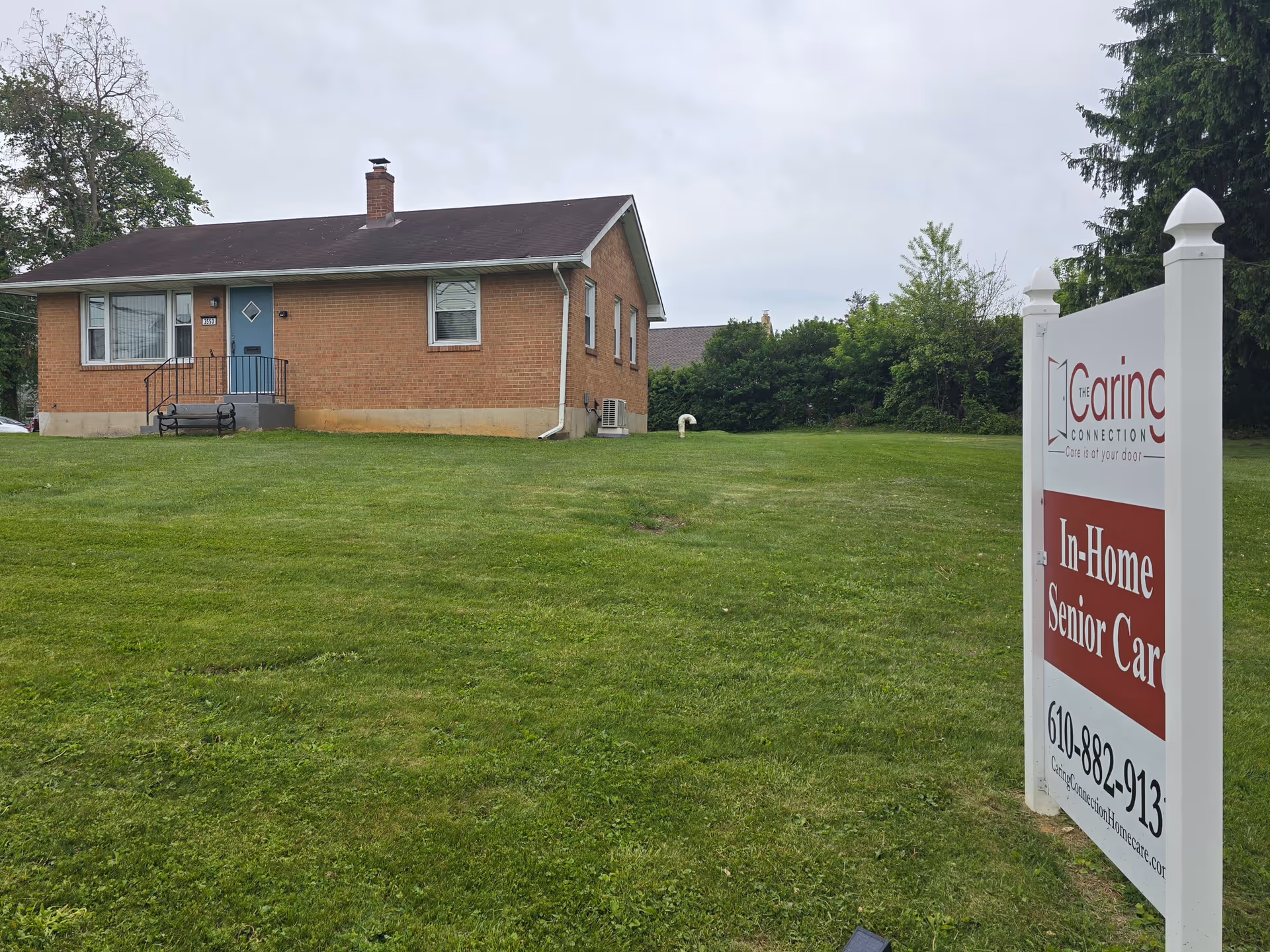 A brick building sits on a grassy lawn beside The Caring Connection sign.