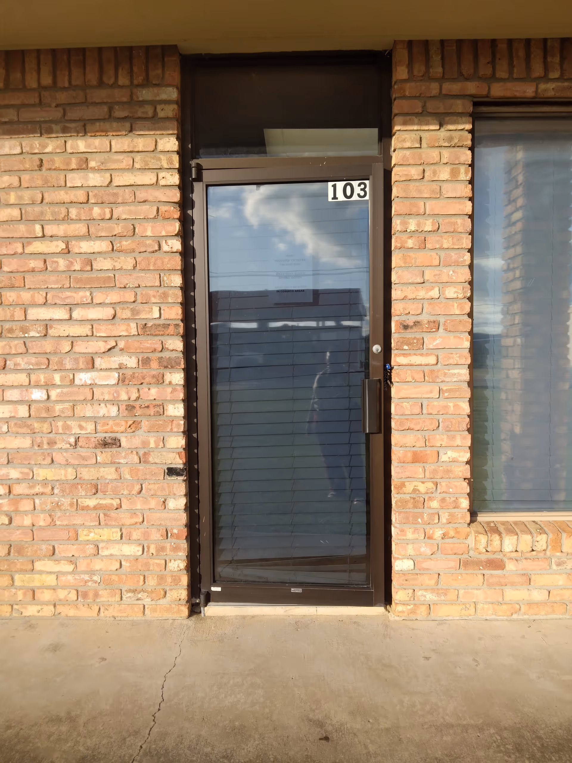Brick exterior doorway with glass door and the number 103 on the frame.