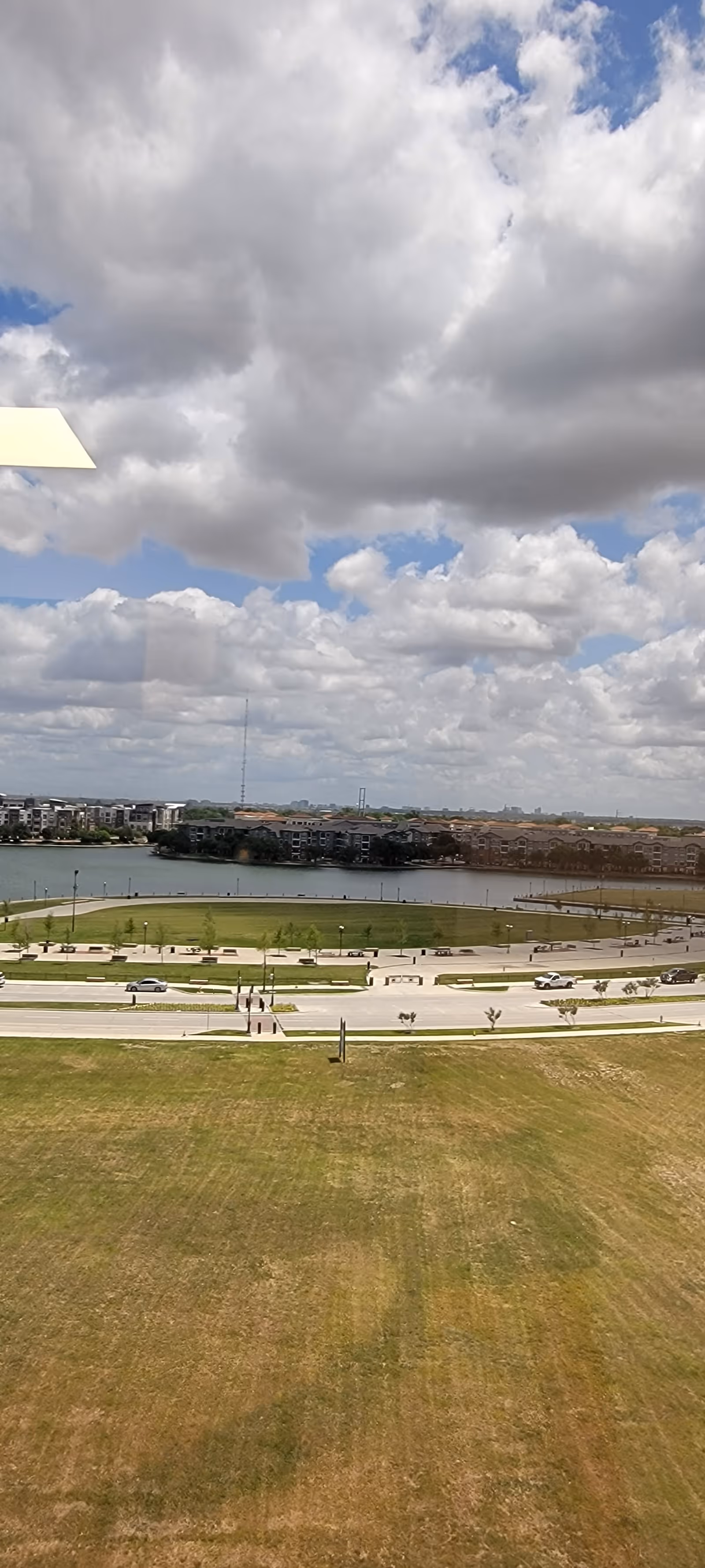 Outdoor view with grassy field, road, lake, and cloudy sky.