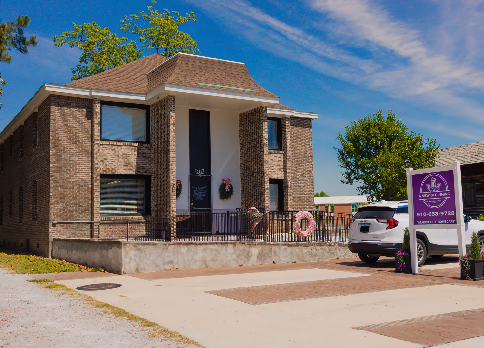Brick senior care facility exterior with entrance, railing, and a parked car.