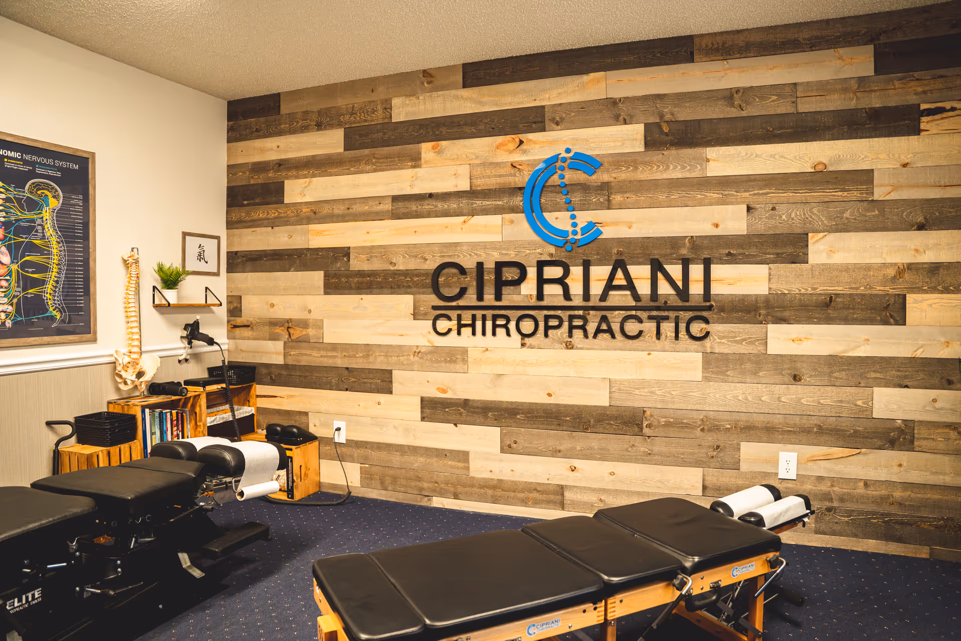 Chiropractic treatment room with exam tables and a wood-paneled wall sign.
