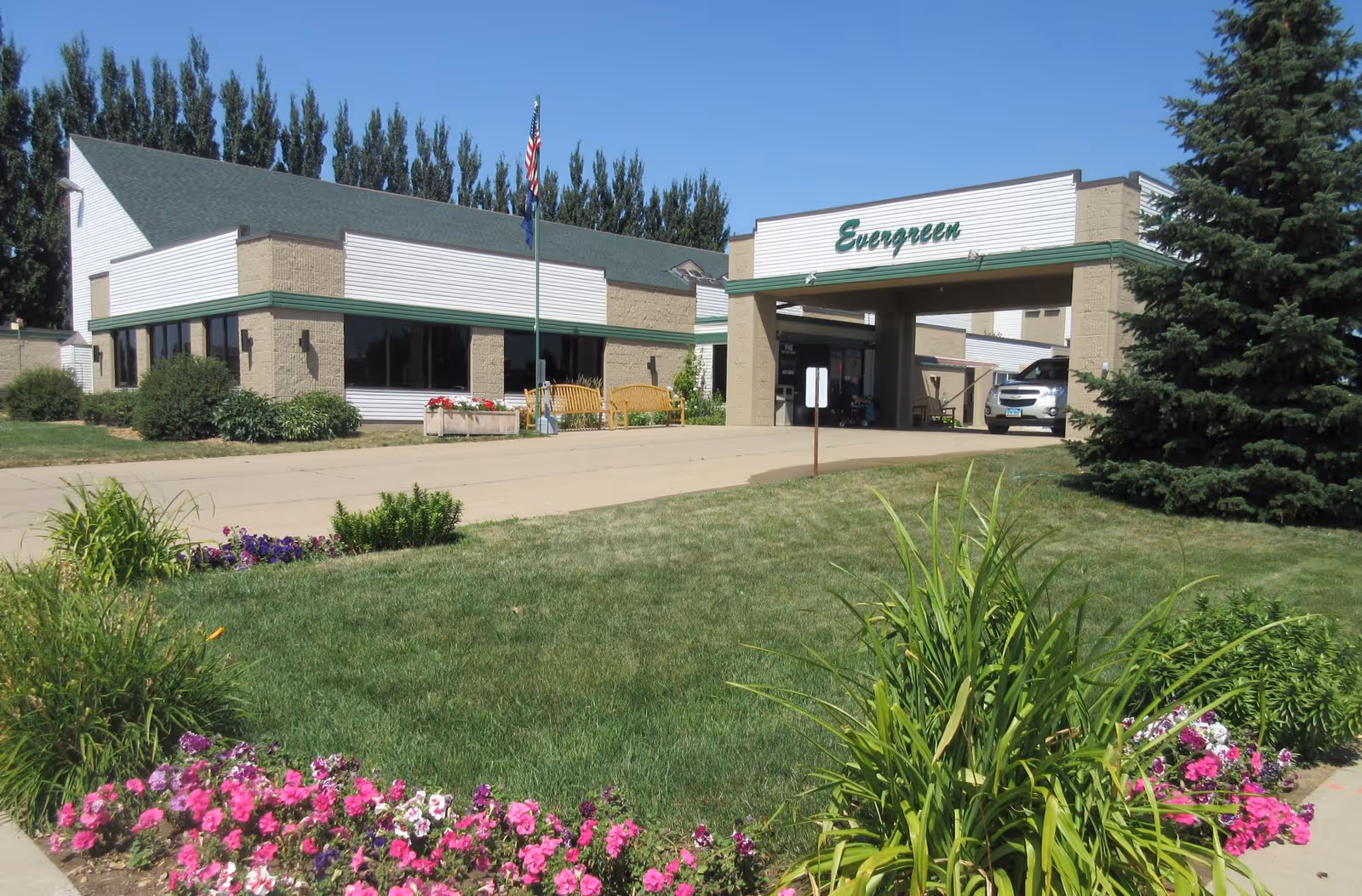 Exterior view of Evergreen senior living facility with entrance, flag, and well-kept landscaping.