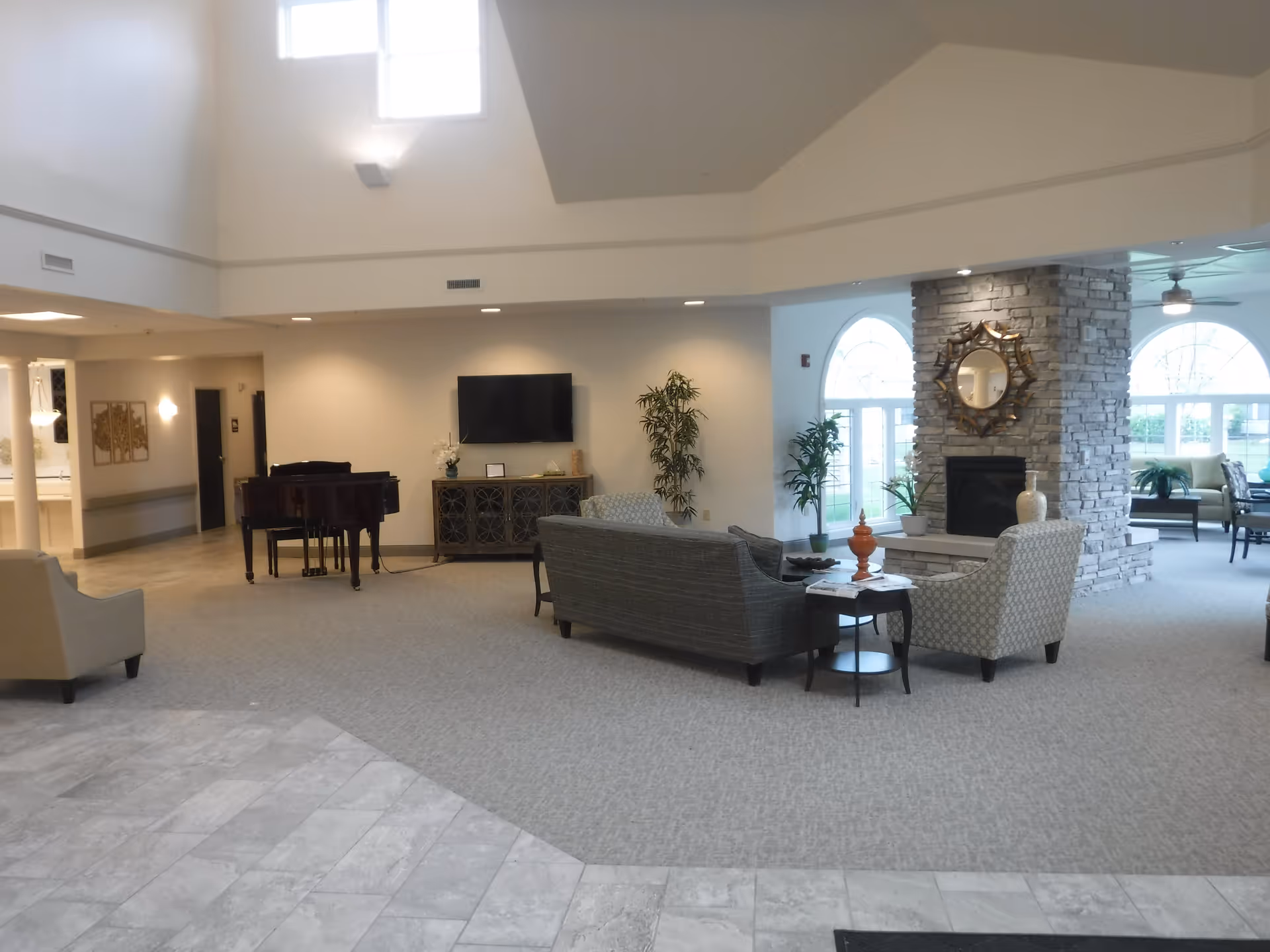 Spacious hotel style lobby with sofas, a stone fireplace, piano, and large arched windows.