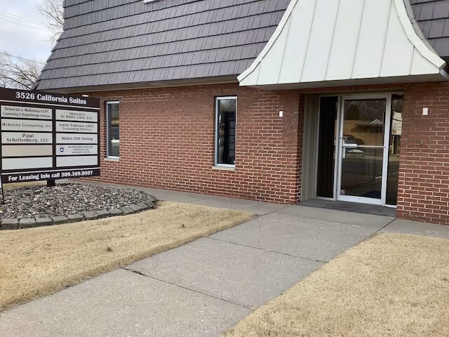 Brick building exterior with glass entrance and a multi-tenant sign near the walkway.