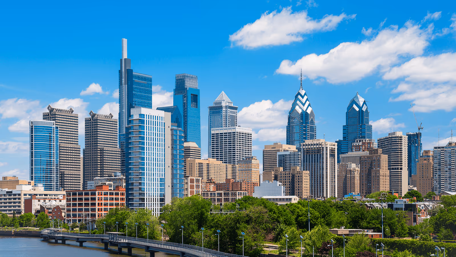 Blue sky over a city skyline with tall buildings and a river.