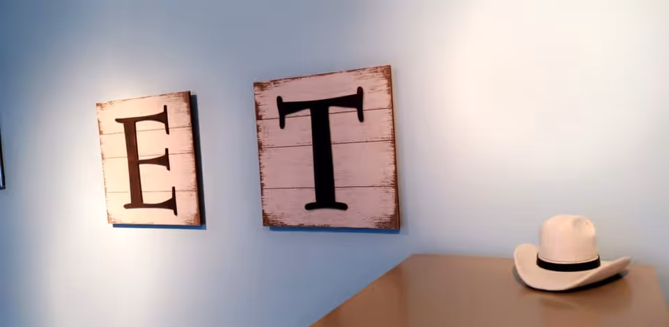 Blue interior wall with rustic ET letter art and a white cowboy hat on a surface.