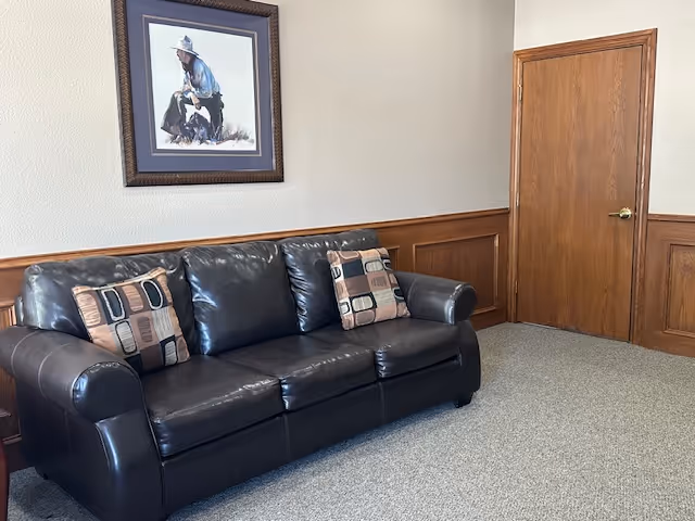 A black leather sofa in a furnished senior living lounge with wall art.