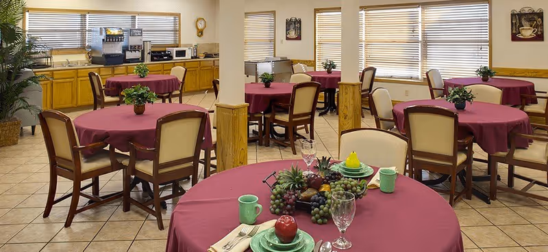 A senior living facility dining hall with magenta tablecloths and round tables.