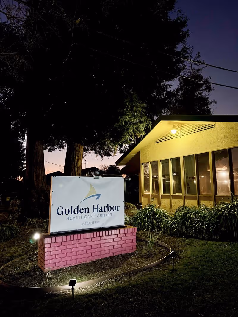 Night exterior of a small yellow building with a lit sign reading Golden Harbor Healthcare Center