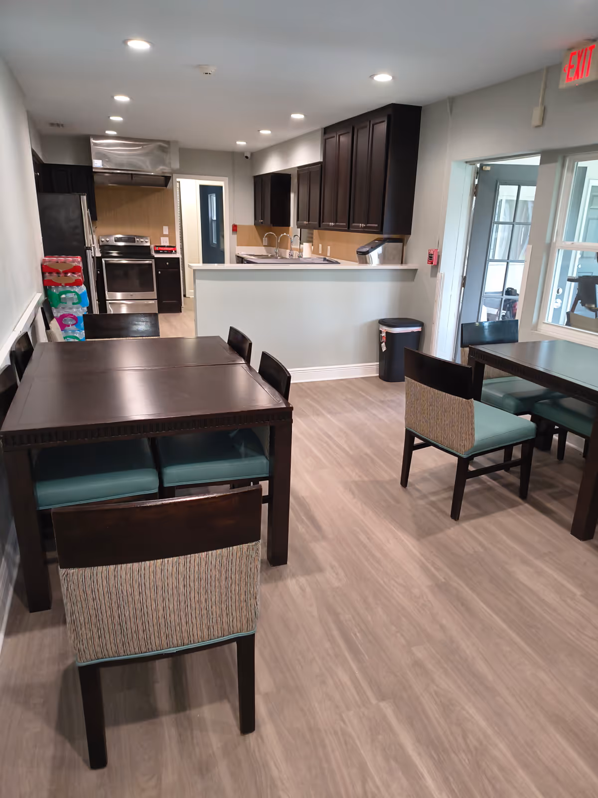 Interior dining area with dark wood tables, teal chairs, and a visible kitchen.