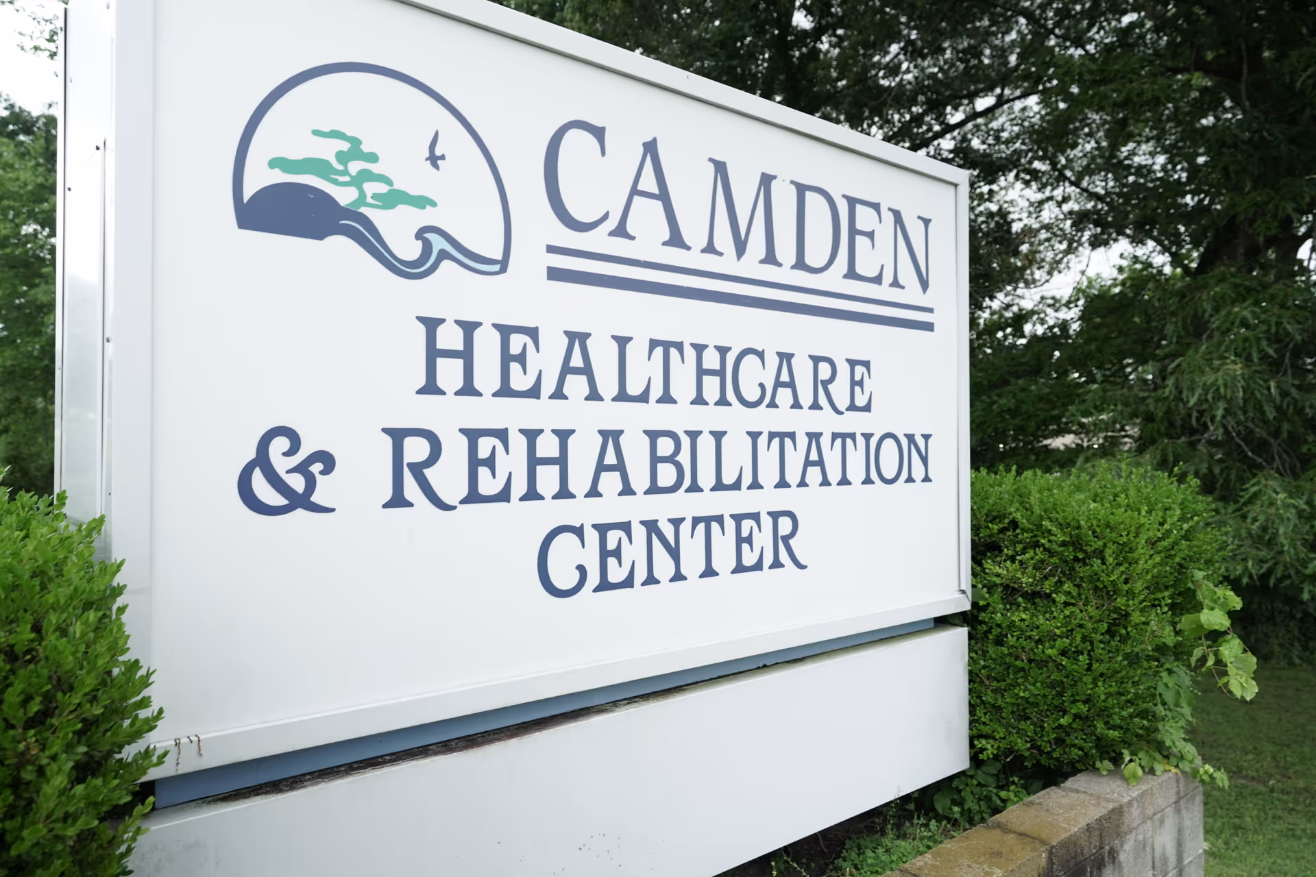 Large outdoor sign reading Camden Healthcare & Rehabilitation Center, surrounded by greenery.