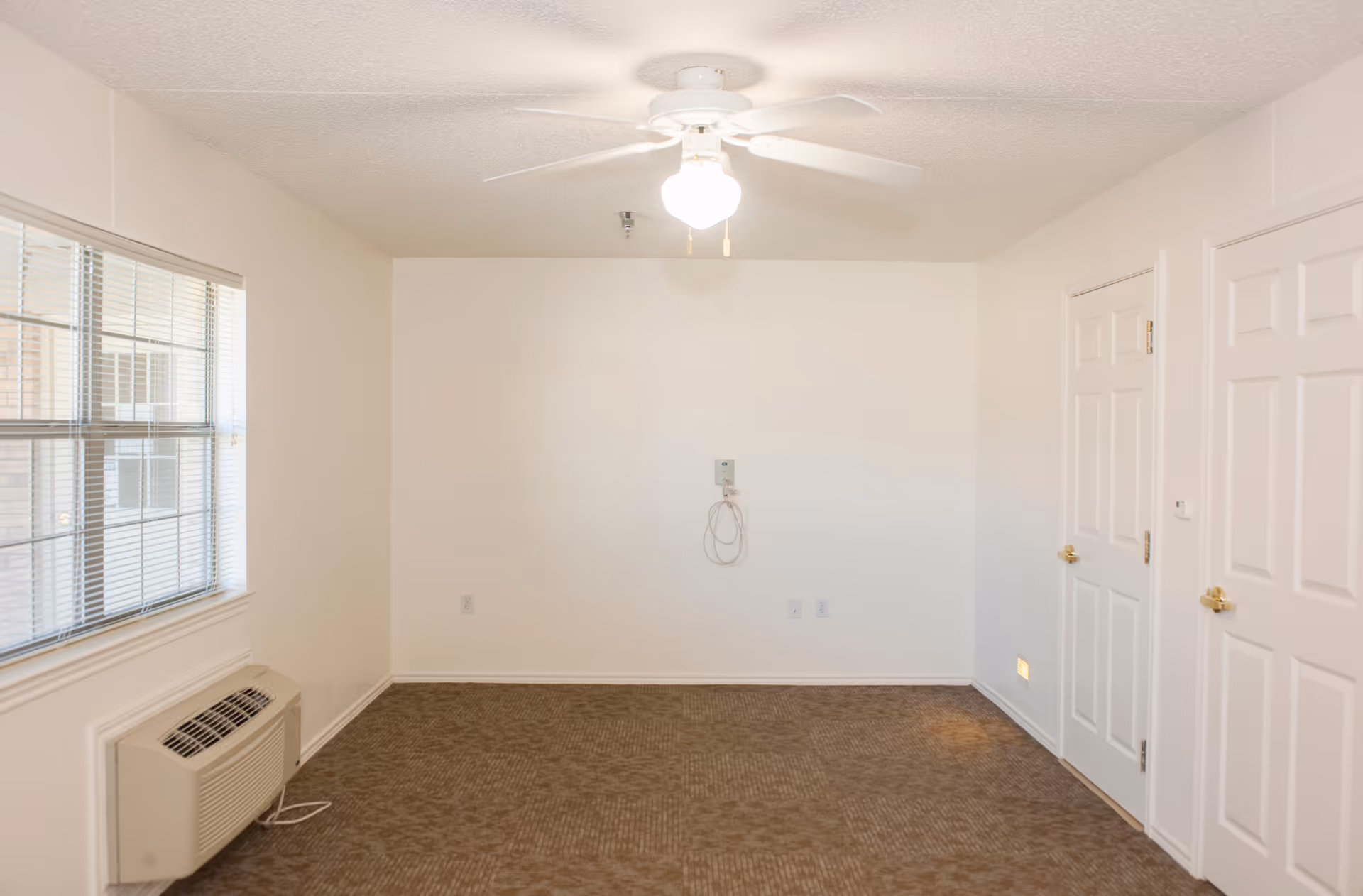 Empty room with a ceiling fan, window, air conditioner, and two white doors.