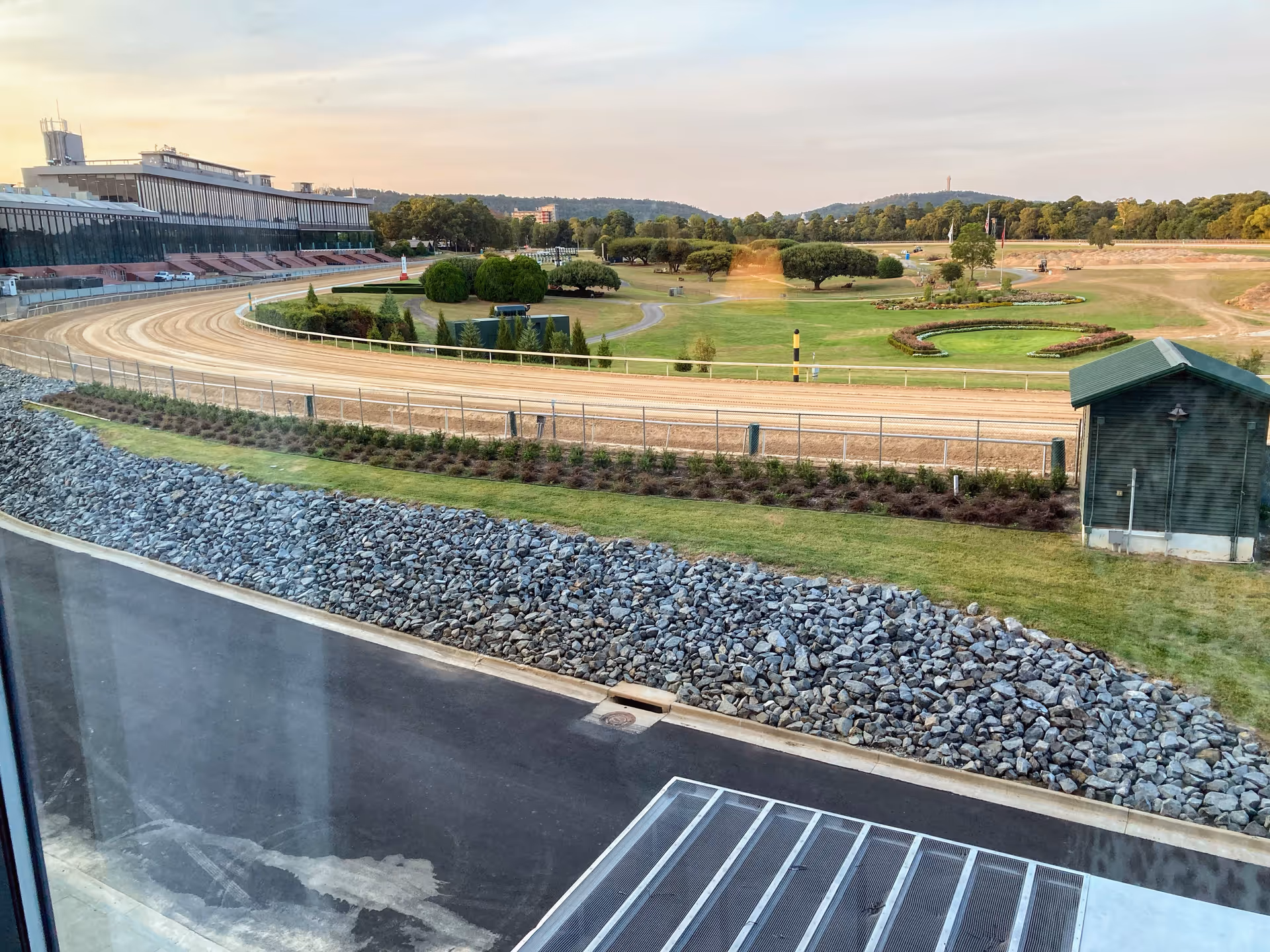 An oval dirt race track bordered by grass and a distant grandstand.