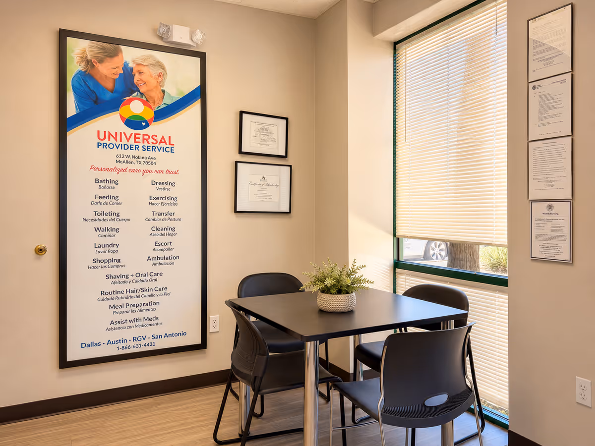 Small interior meeting area with table, four chairs, plant, window blinds, and wall certificates.