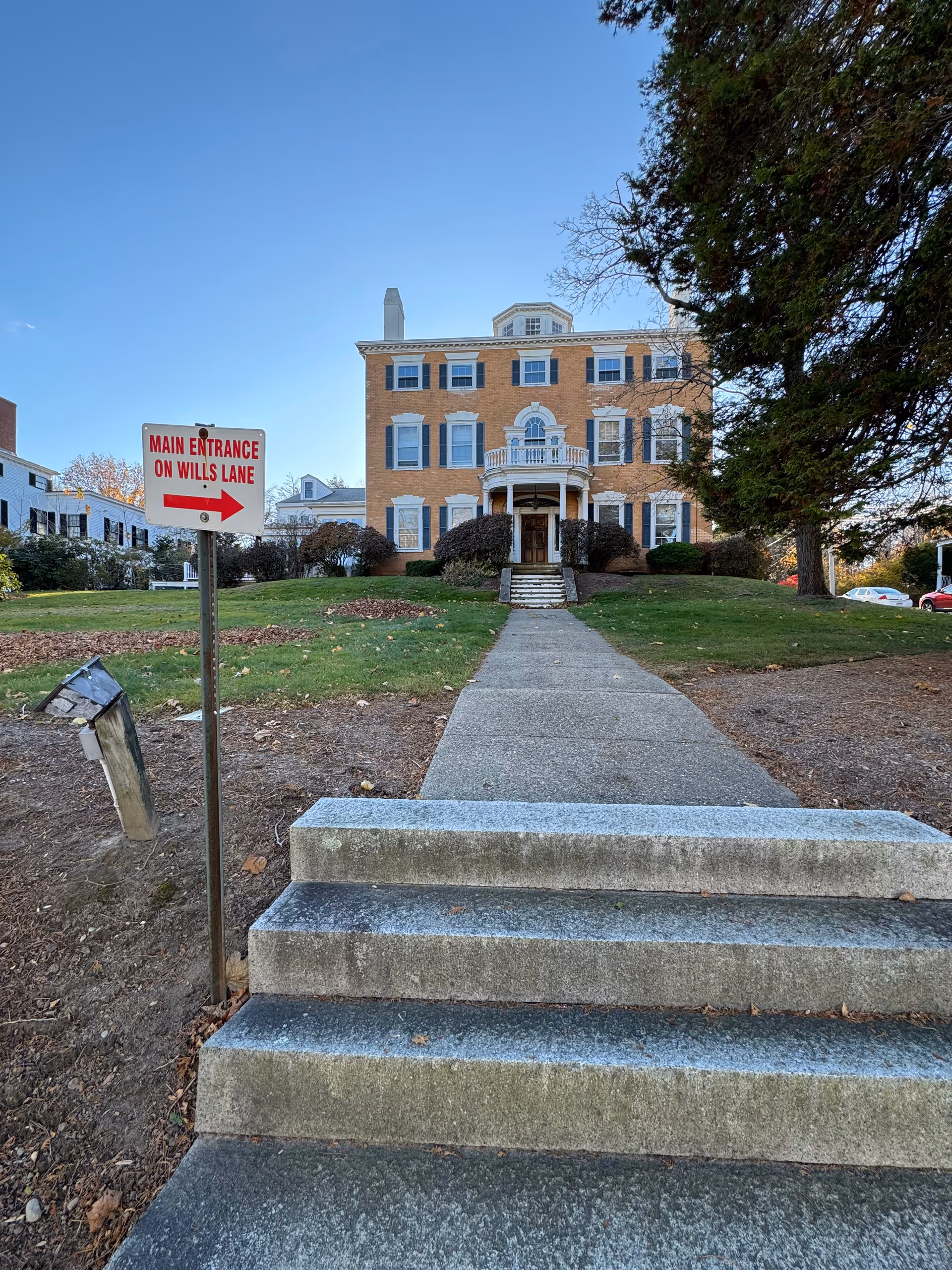 Brick senior living facility front facade with stairs, pathway, sign, and surrounding trees.