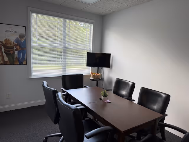 Small conference-style dining room with dark table, chairs, window, and wall poster.