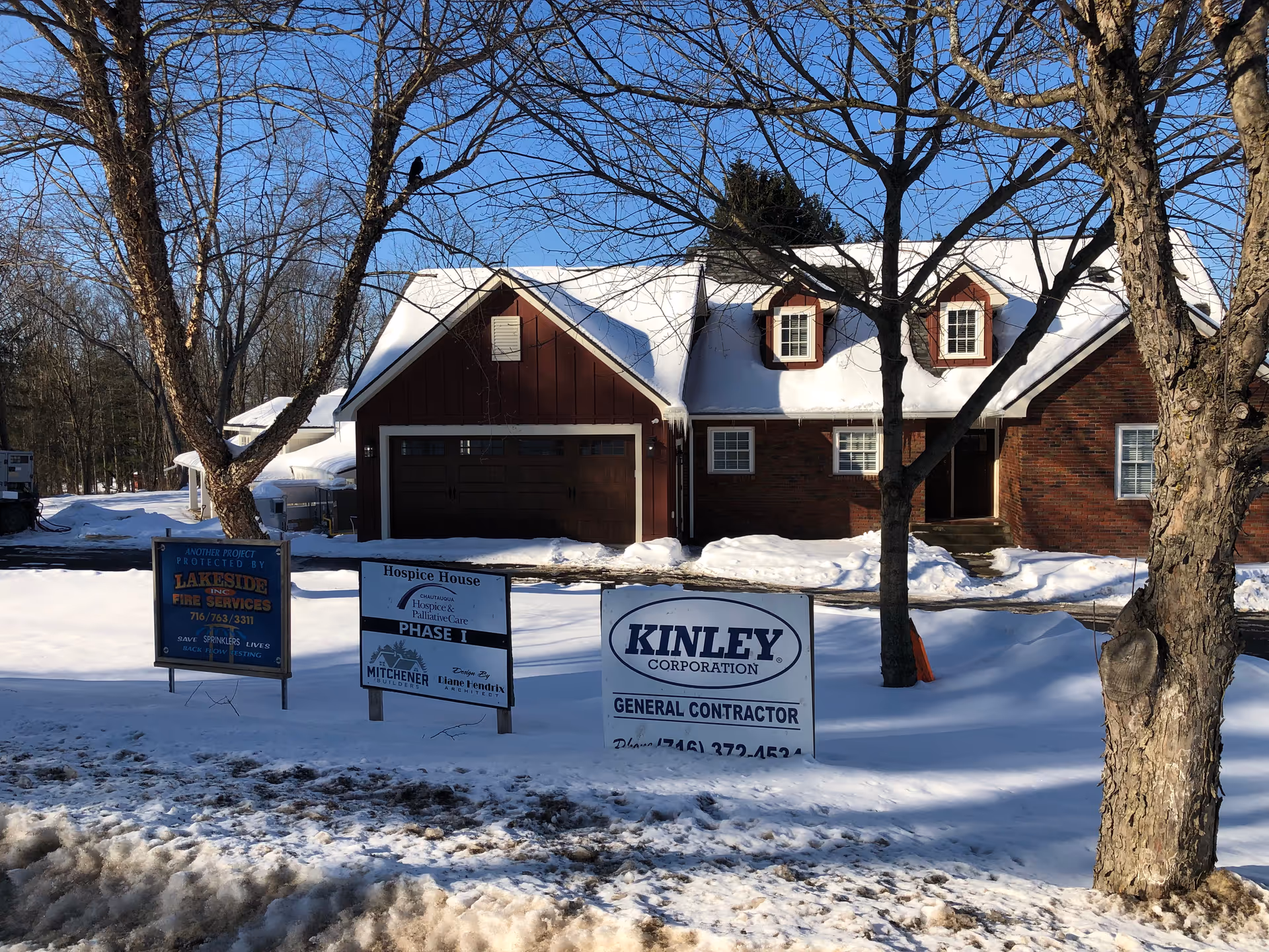 Snow-covered brick hospice-style building with several advertising signs in front.