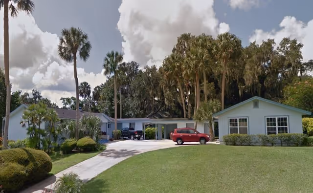 Single-story blue building with driveway, palm trees, and parked cars in front.
