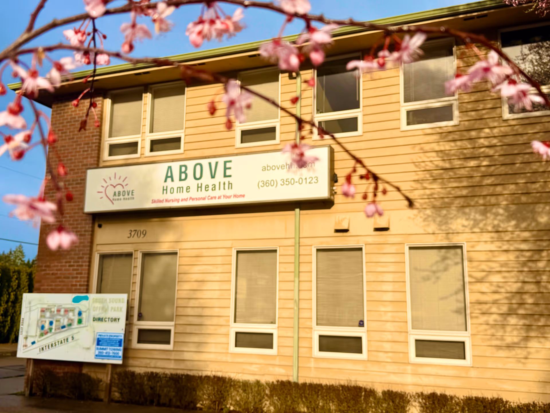 Front view of a building with ABOVE Home Health sign and pink blossoms.