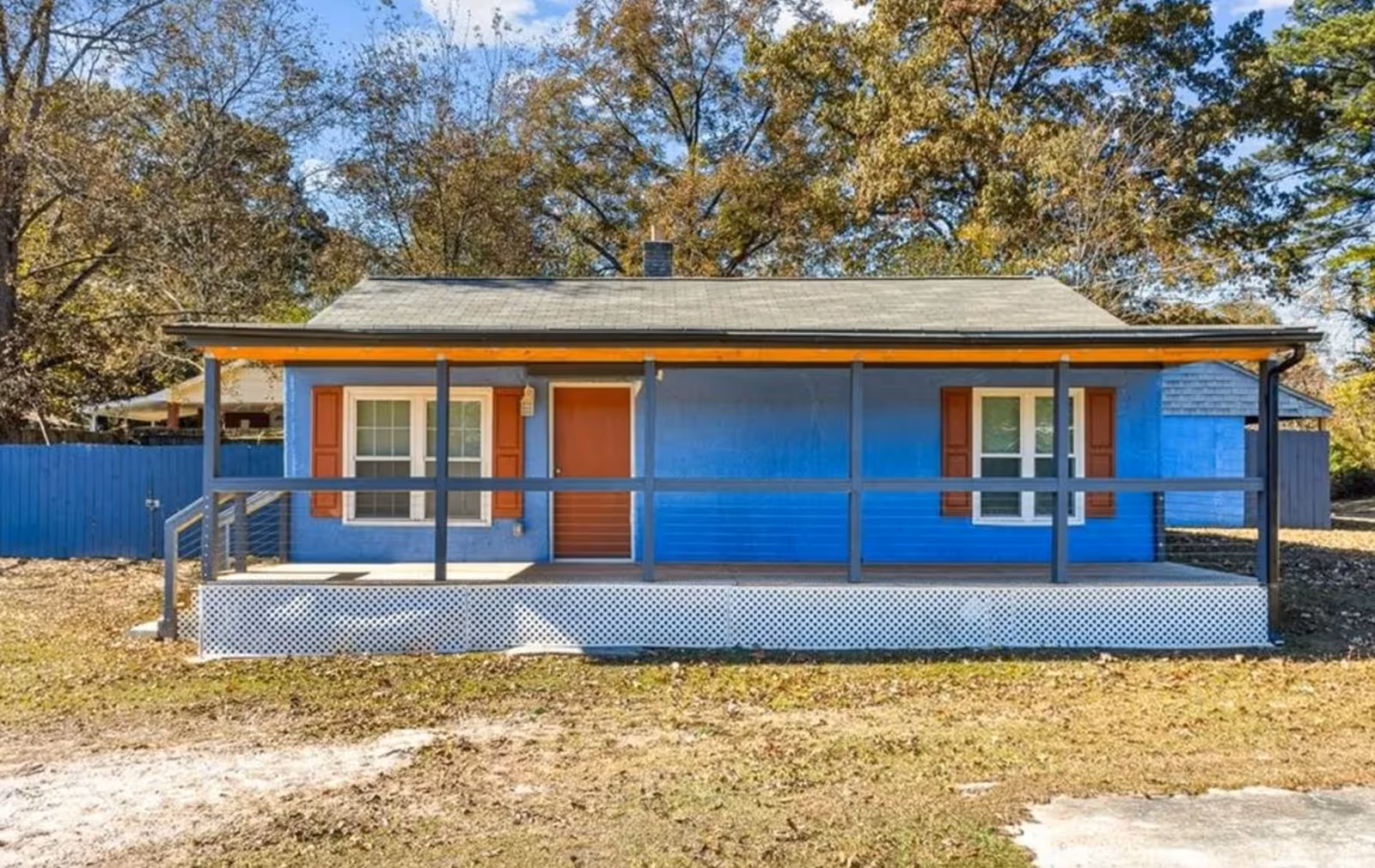 Small blue house with a wooden front porch and railing in a grassy yard.