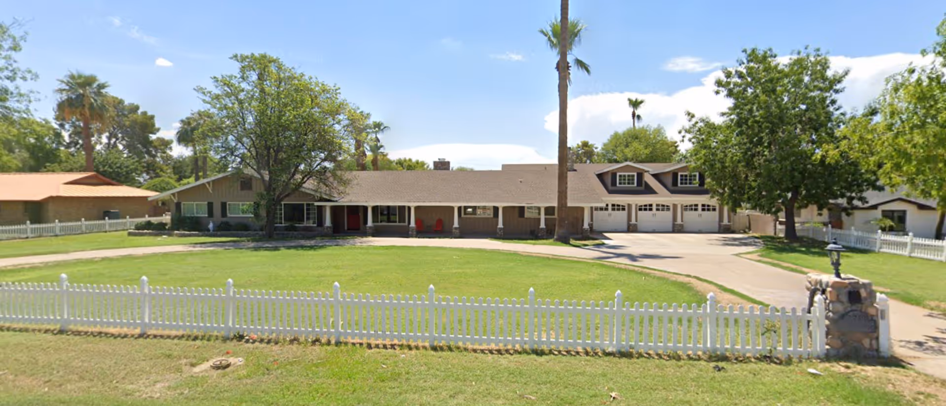 Single-story assisted living facility with a long front lawn, white picket fence, and garages.