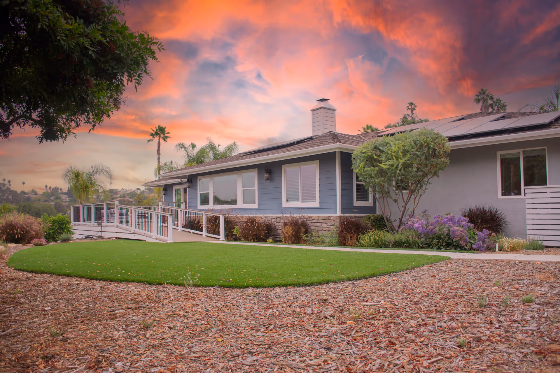 Sunset-lit exterior of a single-story assisted living facility with ramp and landscaped yard.