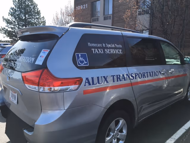 Silver van with Alux Transportation branding parked outdoors beside a building.