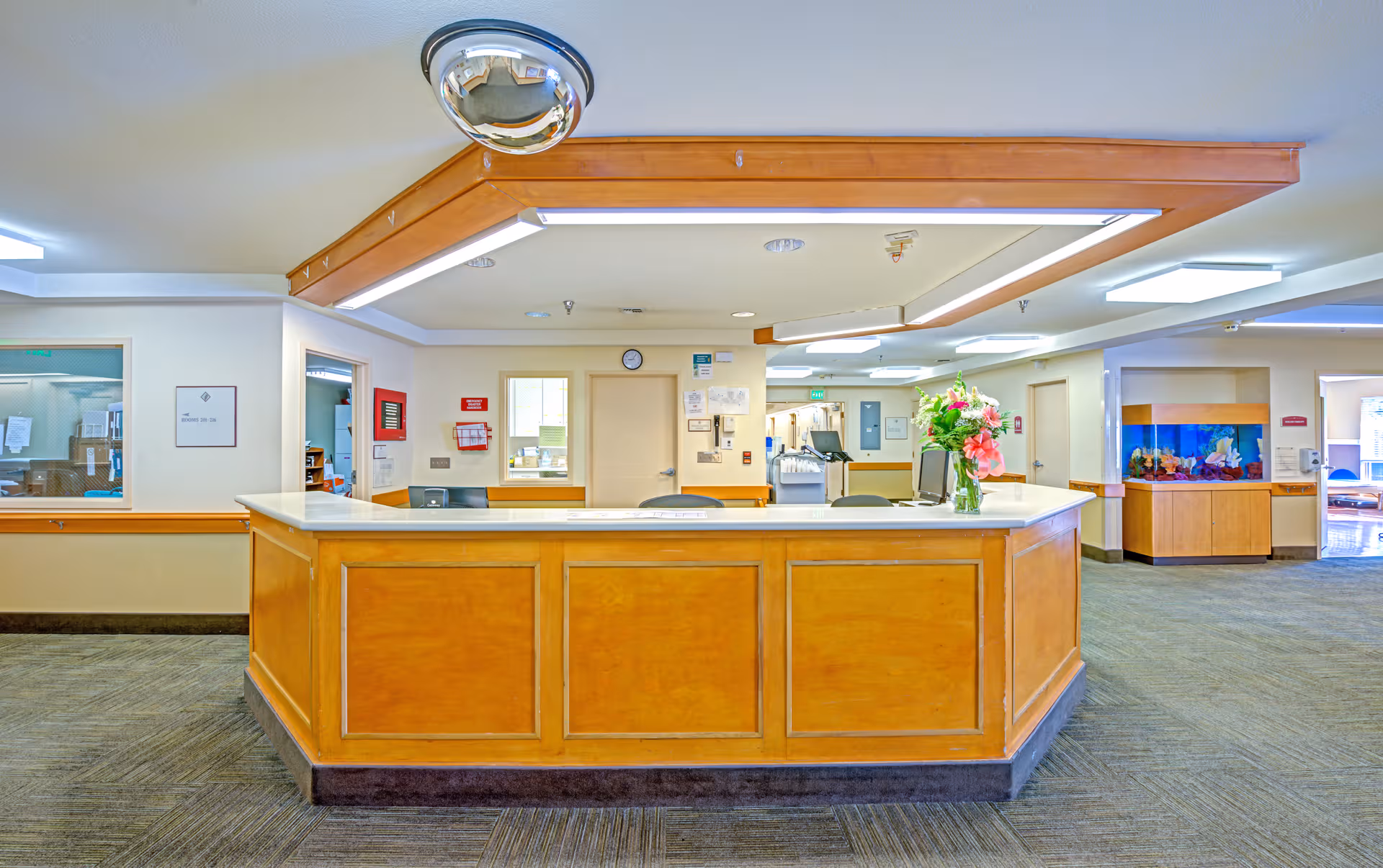 A curved wooden reception desk sits in a bright senior living lobby.