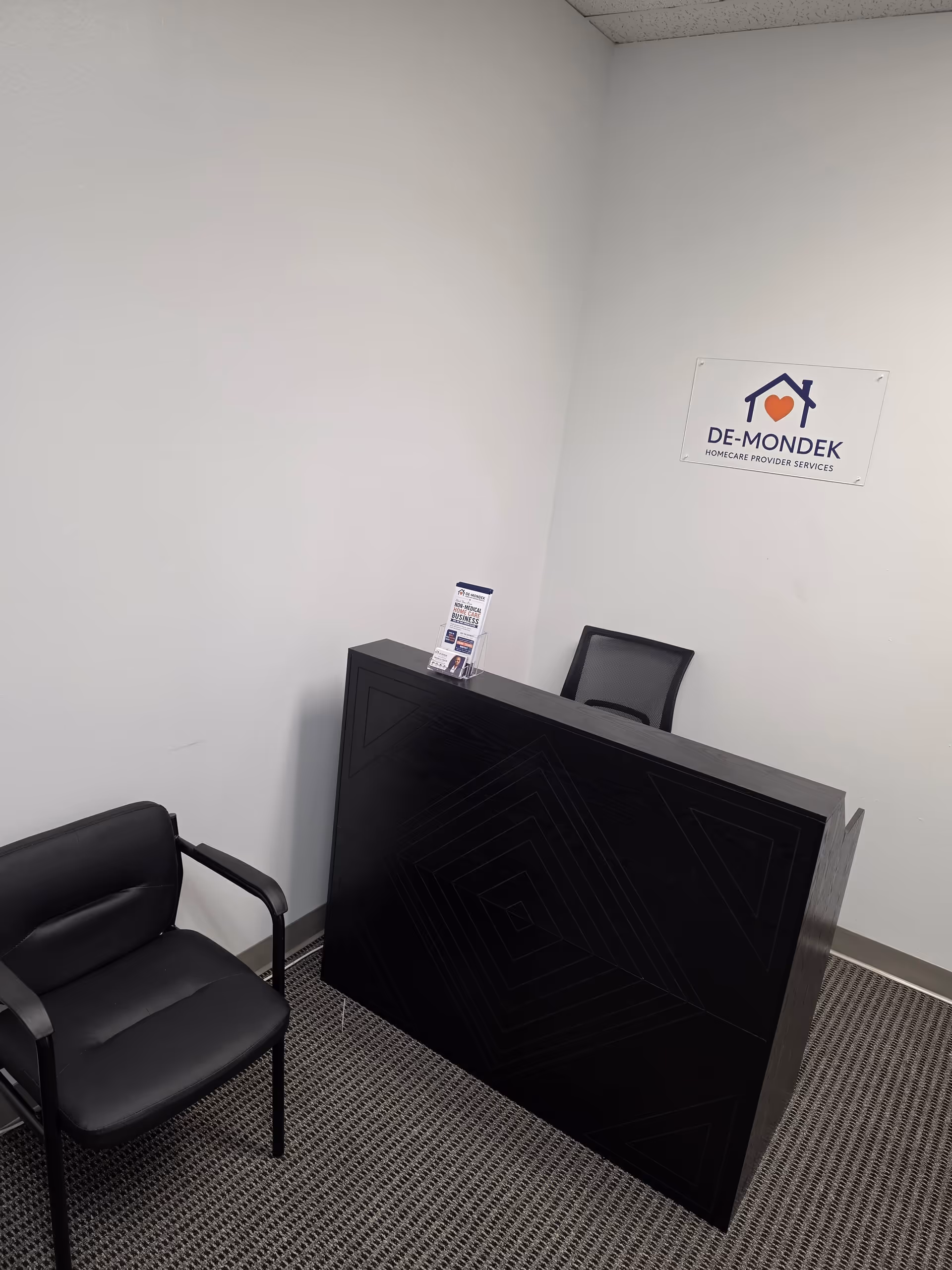 Reception desk in a small room with a De-Mondek Homecare sign on the wall.