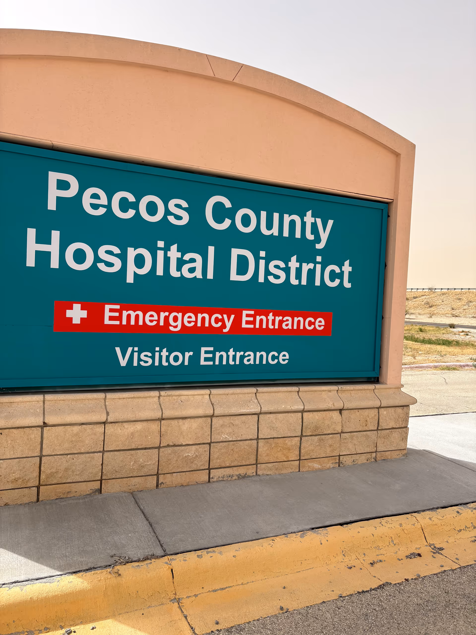 Exterior hospital sign reading Pecos County Hospital District Emergency Entrance and Visitor Entrance.