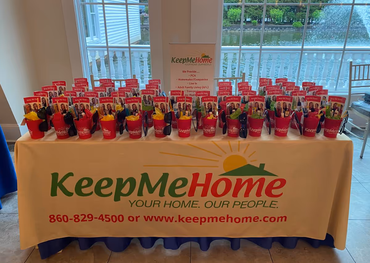Indoor promotional table with KeepMeHome branding and red buckets arranged along the table.