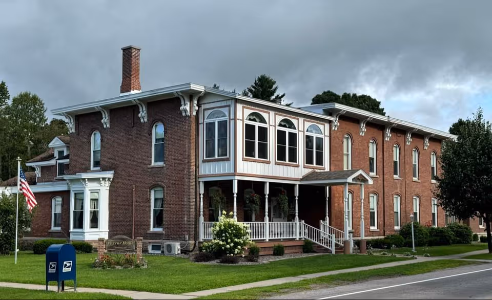 A brick senior living building with a wrap porch, steps, and well-kept lawn.