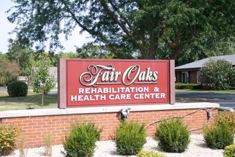 Red Fair Oaks Rehabilitation and Health Care Center sign on brick wall with landscaping and trees.