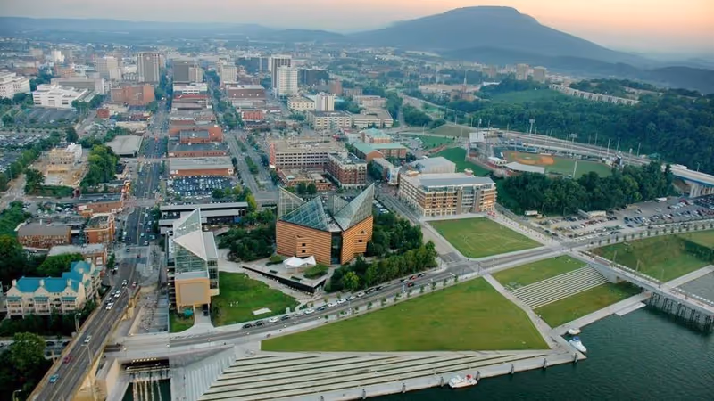 Aerial city view showing modern buildings, green parks, and a waterfront promenade.
