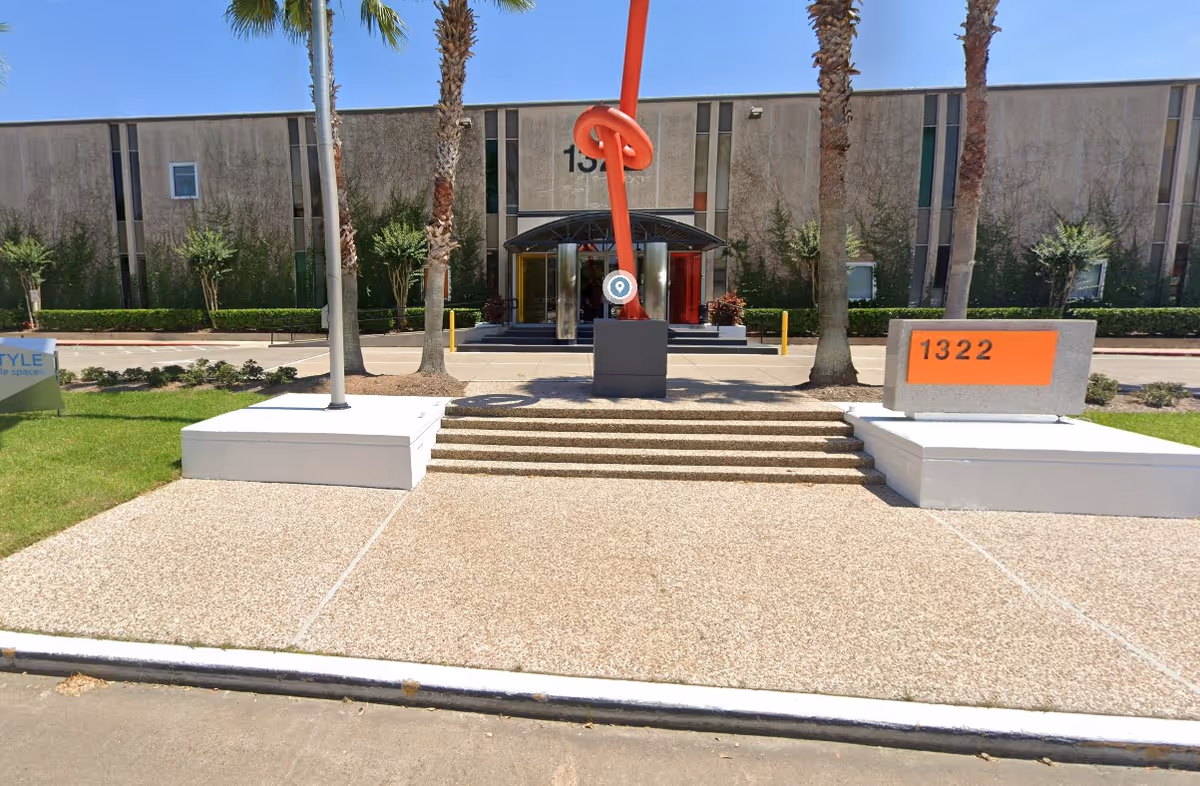 Front view of a beige facility entrance with steps, palm trees, and orange address sign.