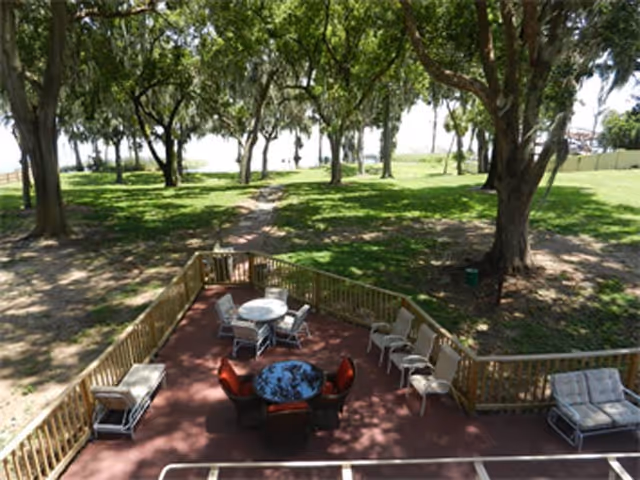Outdoor patio with round table, chairs, and trees on a red deck.