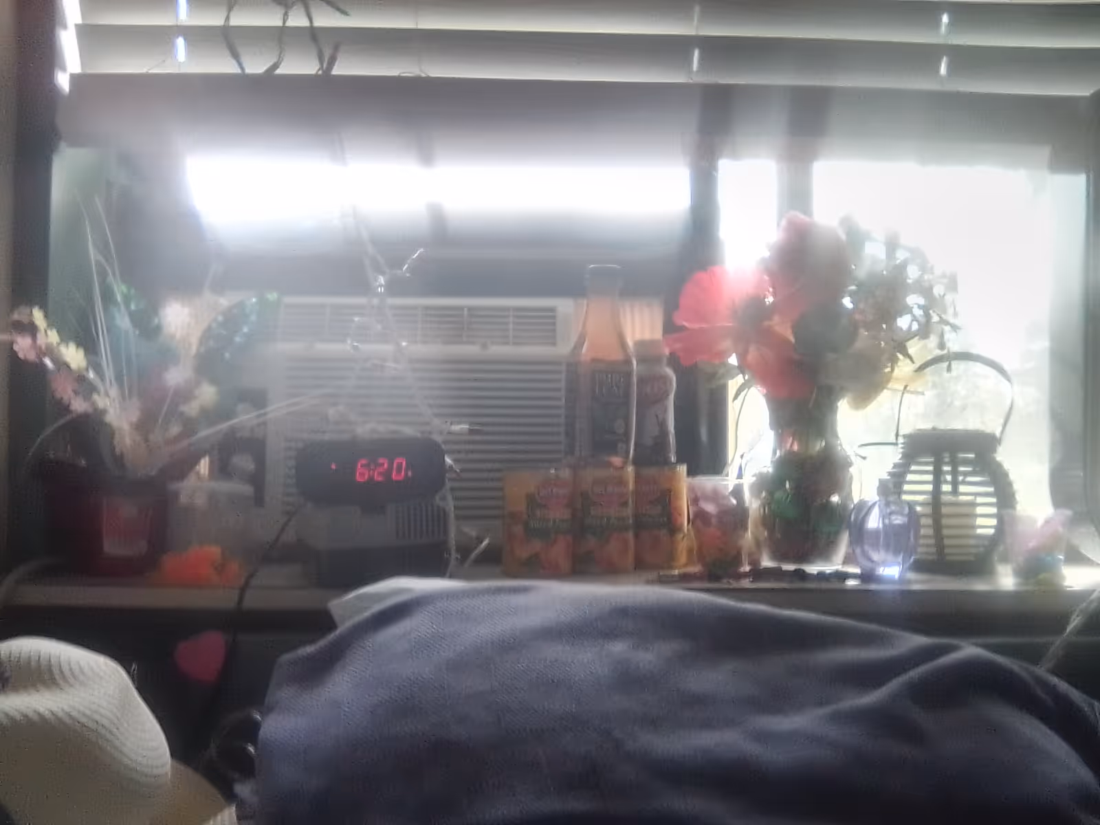 Bedroom scene with windowsill display: flowers, juice boxes, clock, lamp, and a bed.