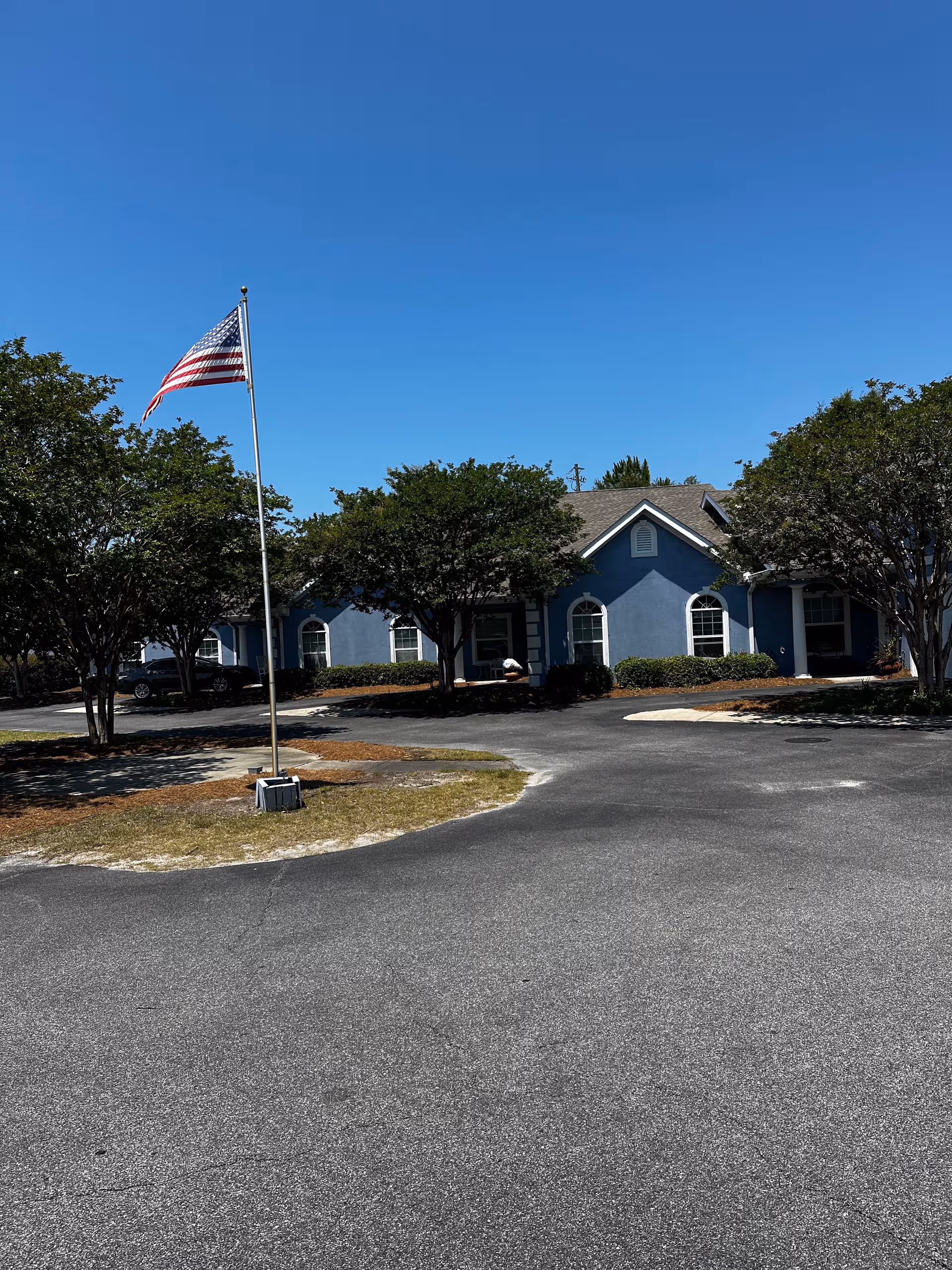 Blue Charter Senior Living building with flagpole and trees in front.