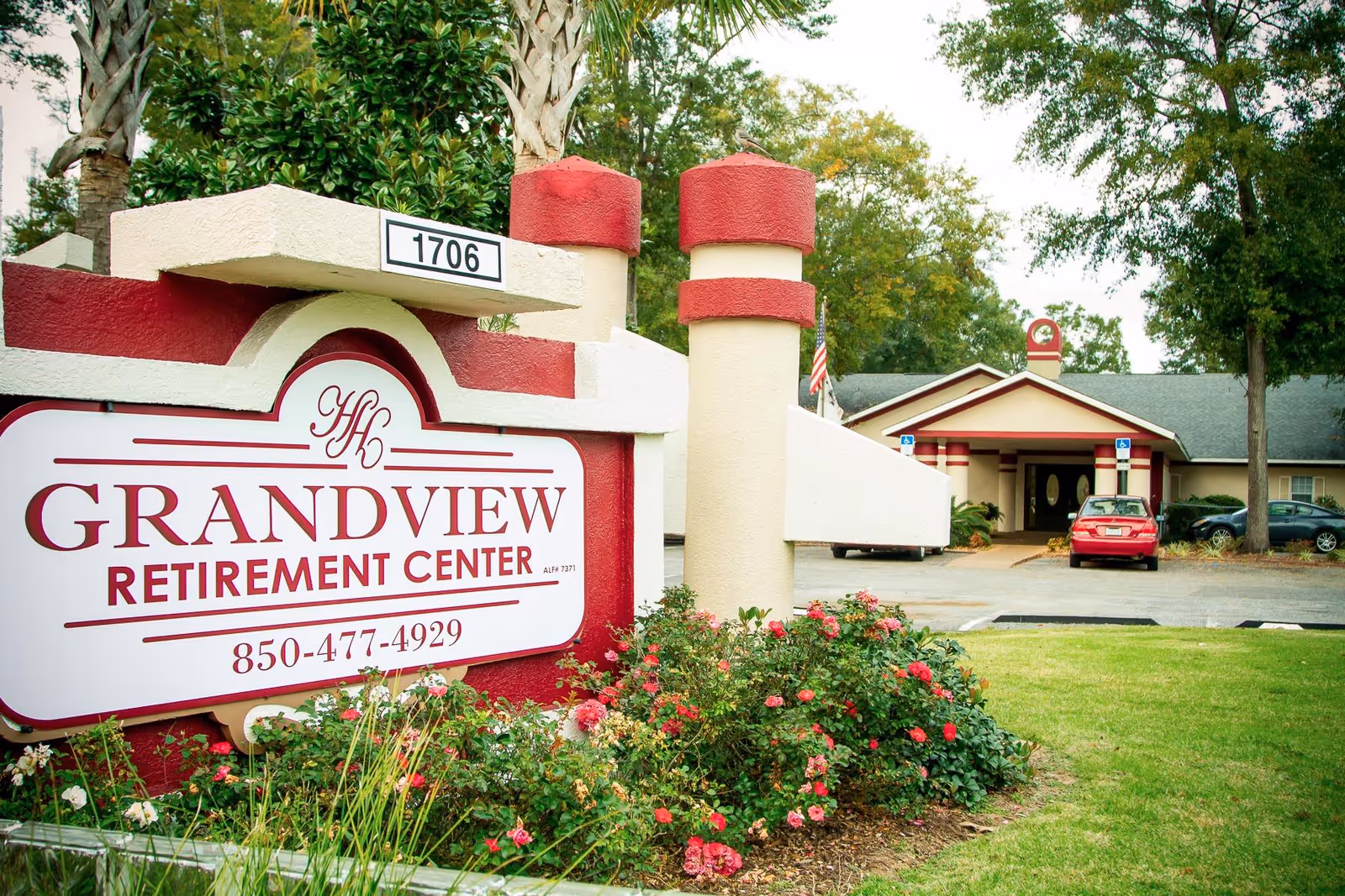 Sign for Grandview Retirement Center in front of landscaped lawn with the facility entrance and driveway visible behind it.
