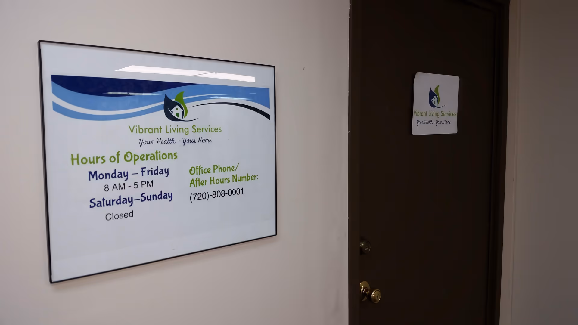 Framed Vibrant Living Services sign beside a dark doorway in an interior hallway.