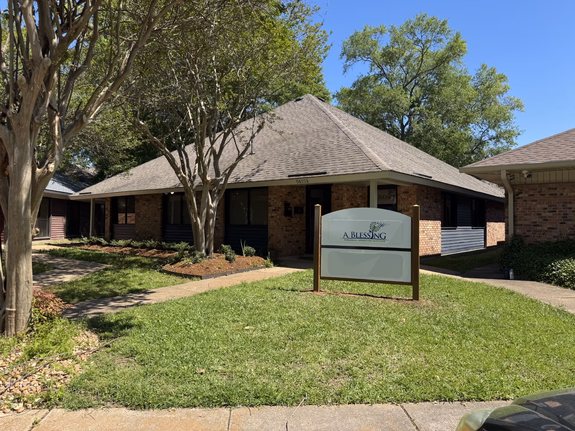 Single-story brick facility exterior with a sign reading A Blessing and surrounding trees and lawn.