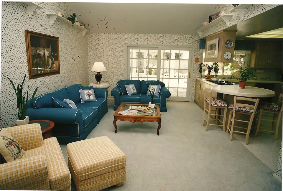 Cozy living room with teal sofas, a coffee table and a checkered armchair, opening to a kitchen with a breakfast bar.
