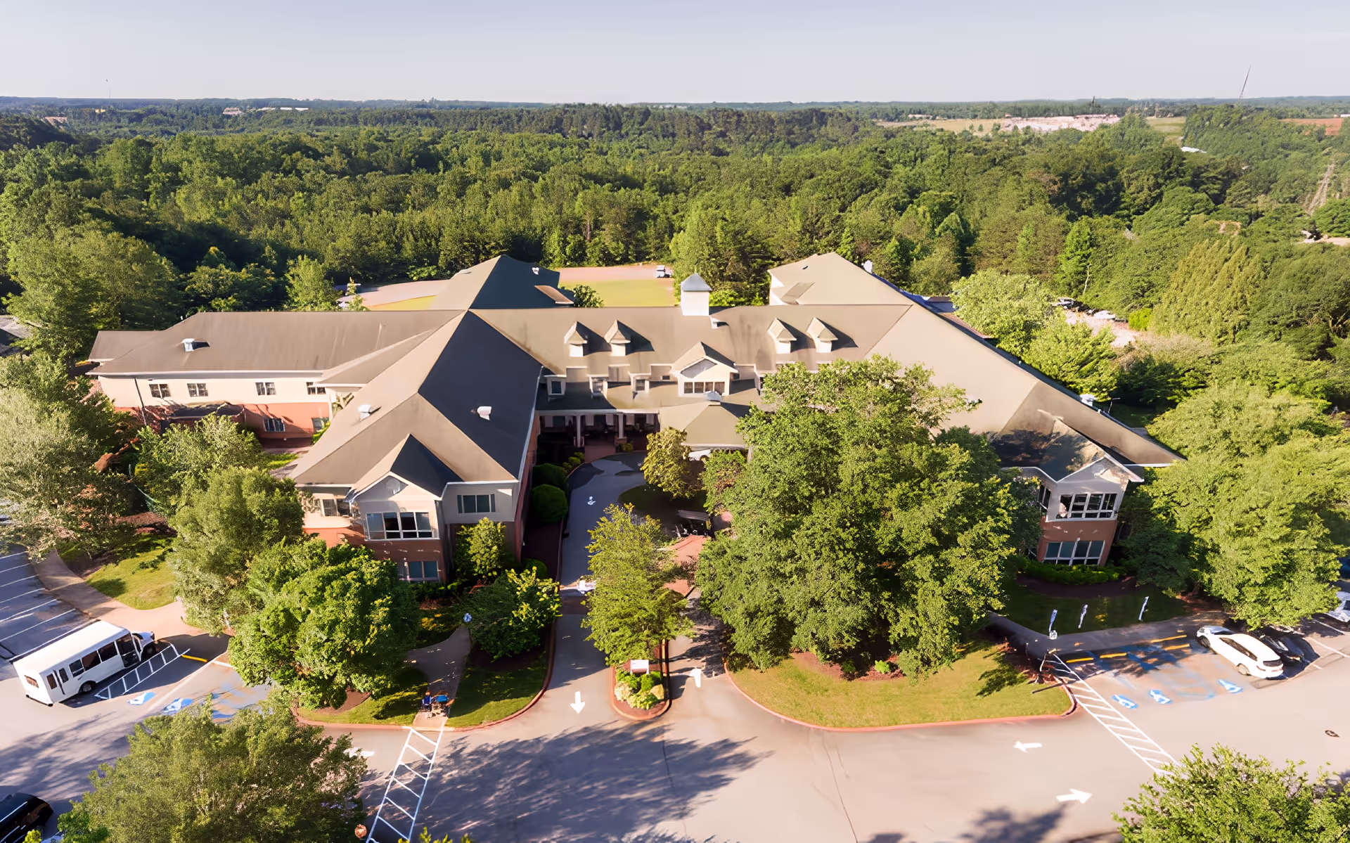 Aerial view of Rosecrest Retirement Community building surrounded by trees and greenery, with a parking lot and driveway visible in front of the facility.
