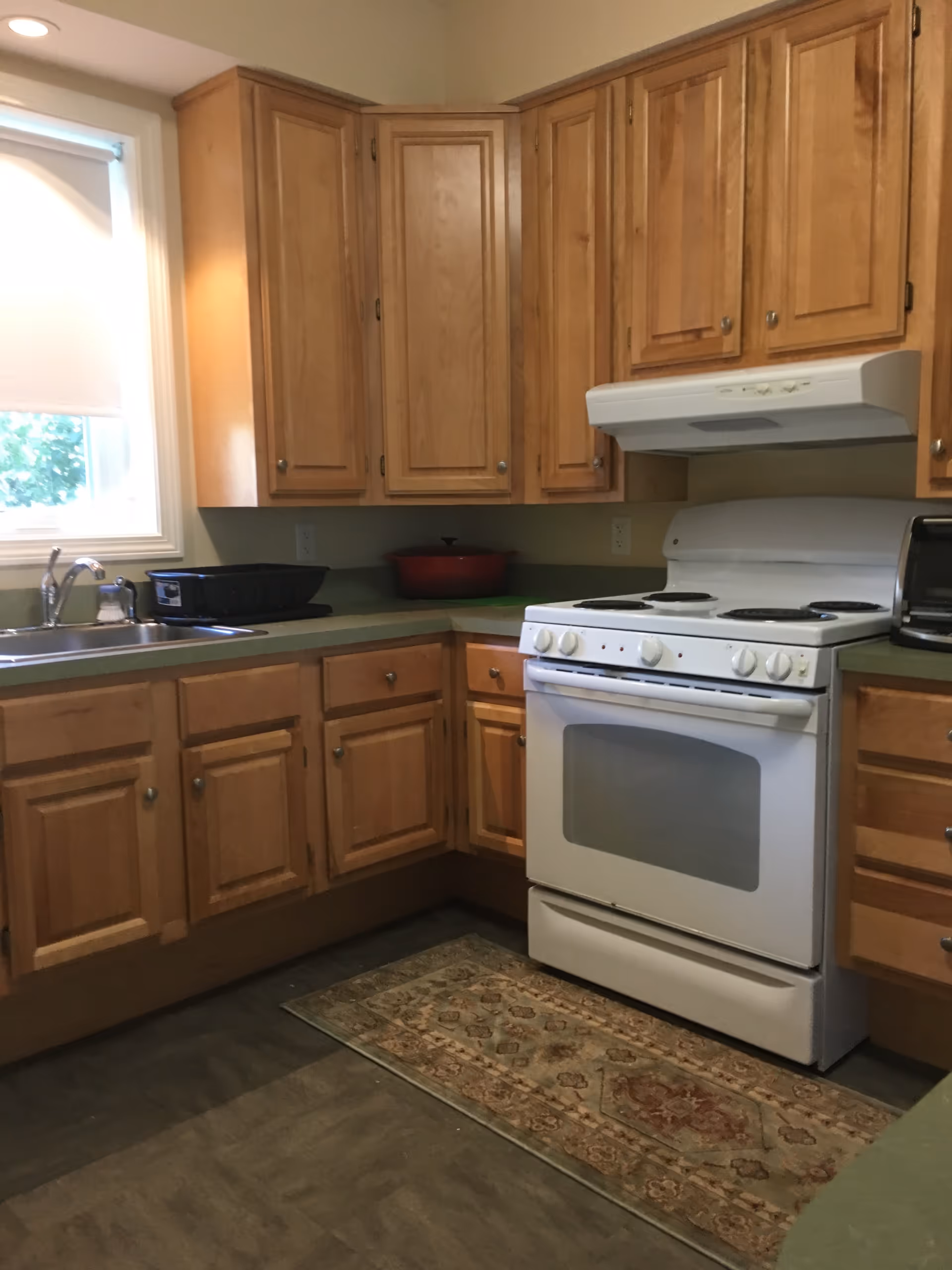 Wooden kitchen cabinets surround a white stove and sink under a window.